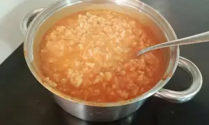Gęsta zupa pomidorowa z ryżem w metalowym garnku, z widoczną łyżką.
