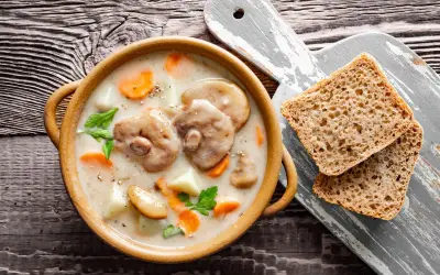Aksamitna zupa z maślaków z kawałkami ziemniaków i marchewki, podana z chlebem na drewnianym stole.