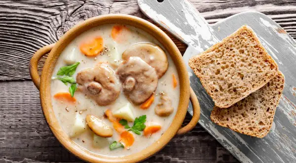 Aksamitna zupa z maślaków z kawałkami ziemniaków i marchewki, podana z chlebem na drewnianym stole.