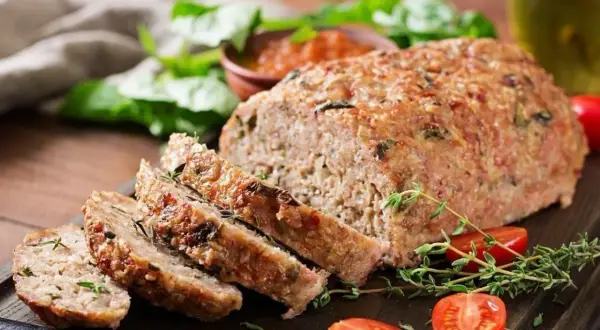 Pyszna pieczeń rzymska Ewy Wachowicz, pokrojona w plastry, podana z pomidorkami i ziołami.