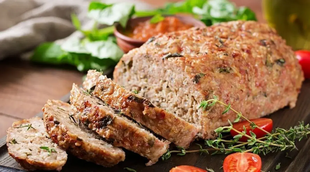 Pyszna pieczeń rzymska Ewy Wachowicz, pokrojona w plastry, podana z pomidorkami i ziołami.