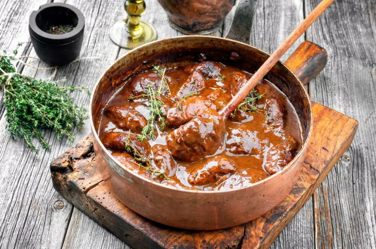 Mięso duszone w sosie własnym, z gałązkami tymianku, w miedzianym rondlu. Idealny przykład, jak dusić mięso, by było soczyste i aromatyczne.